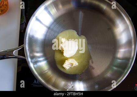 Un portrait de deux morceaux de beurre dans une poêle en acier inoxydable sur une cuisinière à induction. Le produit laitier est en train de fondre pour que le cuisinier puisse en frire Banque D'Images