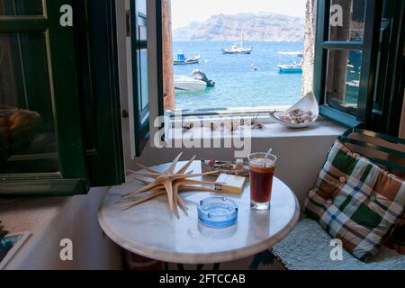 Vue depuis la fenêtre sur la mer à Amoudi, la maison de pêcheur confortable avec des étoiles de mer et un verre sur la table. En arrière-plan la caldeira du volcan Banque D'Images