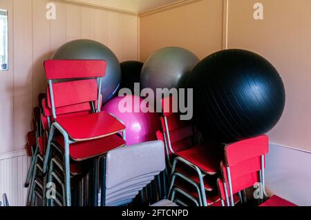 Plusieurs balles de gym colorées sont stockées derrière des chaises encadrées en acier situé dans le hall d'une ancienne école de village construite pour Lady Waterford en 1860, Banque D'Images