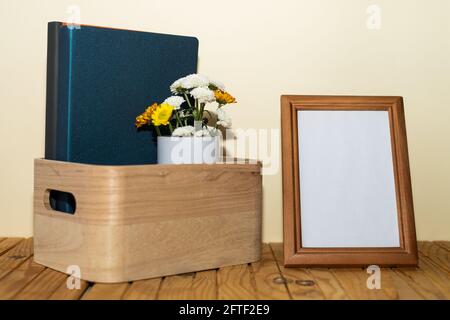 Composition sur table en bois: Boîte avec livres, vase de fleurs et cadre photo avec fond blanc Banque D'Images