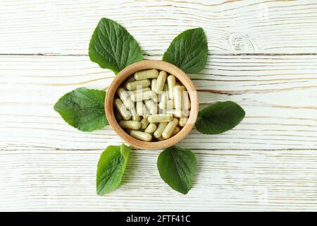 Bol avec des capsules de plantes et des feuilles sur fond de bois blanc Banque D'Images