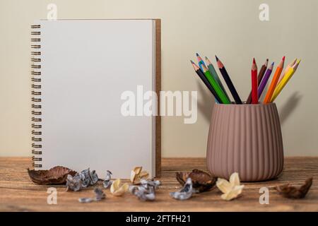 Cahier spirale ouvert avec feuille blanche, crayons de couleur dans le verre à côté et décorations sur la table Banque D'Images