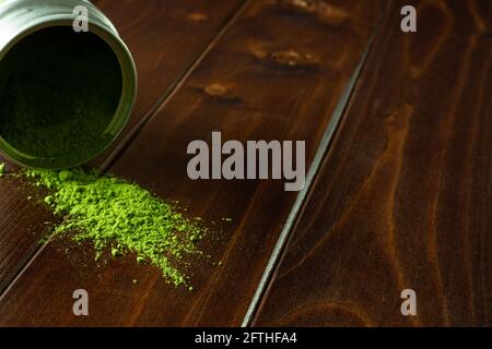 Poudre de matcha tombant de l'étain métallique sur du bois sombre ; gros plan de la poudre de thé vert japonais Banque D'Images