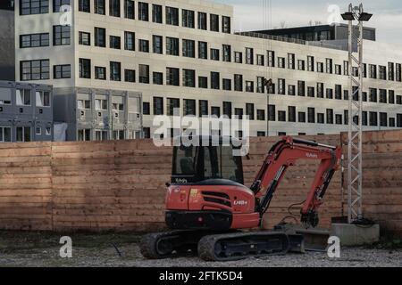 Un creuseur de construction devant une clôture en bois.Derrière elle un nouveau bâtiment. Banque D'Images