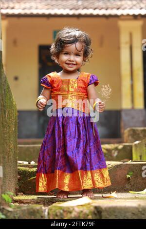 Petite fille indienne du Sud portant belle robe traditionnelle jupe longue et chemisier, assis sur les longs marches d'une maison couverte de champignons verts de mousse. Banque D'Images