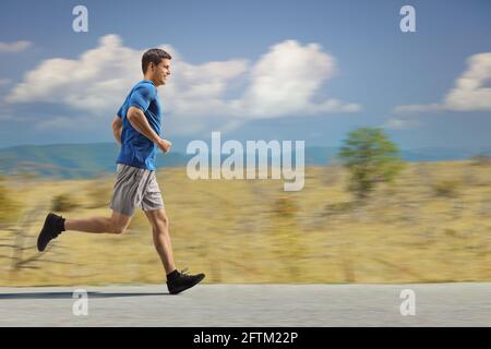Photo pleine longueur d'un type en vêtements de sport courir dans une zone rurale sur une route asphaltée Banque D'Images