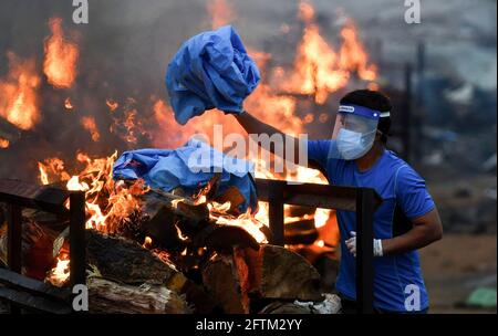 Bengaluru, Inde. 10 mai 2021. Un membre de la famille d'une victime Covid-19 dispose de son EPI usagé dans le pyre après avoir effectué des rituels dans la carrière. La deuxième vague de la pandémie de Covid-19 a pris le système de santé du pays sur le dos, le nombre de victimes augmentant de façon exponentielle, entraînant des crématoriums à fonctionner jour et nuit. Bengaluru a converti l'une de ses carrières inutilisées à Giddenahalli, situé dans la banlieue, en un crématorium ouvert. Crédit : SOPA Images Limited/Alamy Live News Banque D'Images