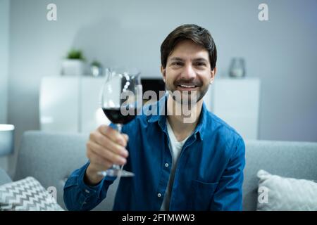 Homme Drinking Red Wine en vidéoconférence à la maison Banque D'Images