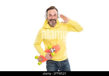 un homme souriant et expérimenté écoute de la musique isolée sur blanc. un homme en pull à capuche jaune avec planche à roulettes. Banque D'Images