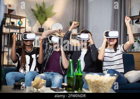 Des personnes gaies et diverses portant des lunettes virtuelles sans fil et s'amusant ensemble à la maison. Concept d'amitié, de divertissement et de technologie numérique portable. Banque D'Images