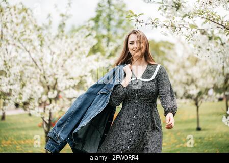 Active fille dans le verger de pomme en fleur en robe rétro et veste en denim. Activité de style de vie en extérieur. Banque D'Images