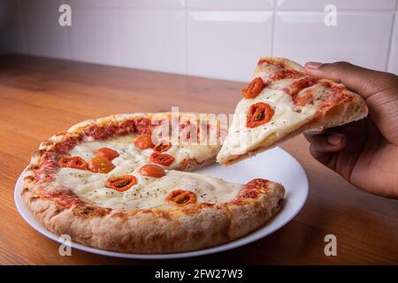 Tranche de pizza levée d'une main. Photo gastronomique Banque D'Images