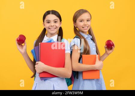 Les élèves heureux avec des livres contiennent des pommes bio vitamine fond jaune, petit déjeuner à l'école Banque D'Images