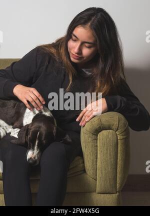 Portrait d'une adolescente souriant et pétant son chien de petit-chien noir et blanc sur un canapé dans son salon. Concept d'amour pour les animaux de compagnie Banque D'Images