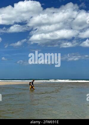 Un homme marche à travers une rivière qui rencontre l'océan Pacifique à Tamarindo, au Costa Rica. Banque D'Images