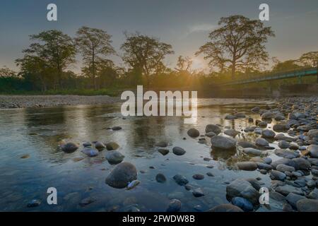 Magnifique lever de soleil sur la rivière Murti, lit de rivière en premier plan avec eau et pierres fluides. Beauté pittoresque du paysage des Dooars, Bengale occidental, Inde Banque D'Images