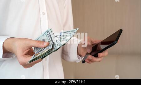 Une personne utilisant des paiements mobiles et des services bancaires mobiles. Un homme détient de l'argent et un smartphone pour les affaires et les achats en ligne. Banque D'Images