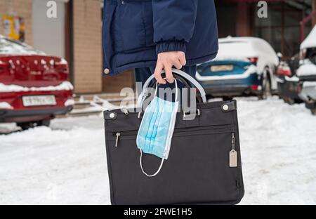 Homme avec un porte-documents et un masque chirurgical, gros plan d'un jeune homme tenant un porte-documents et un masque chirurgical dans sa main Banque D'Images