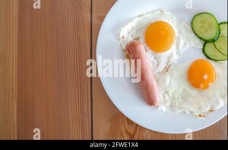 Œufs frits de deux œufs avec concombres et saucisses pour le petit déjeuner. Œufs frits, côté ensoleillé sur une assiette. Concept d'alimentation saine. Banque D'Images