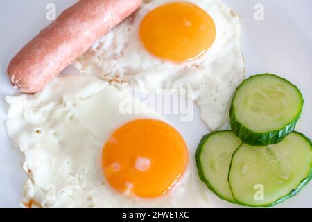 Œufs frits de deux œufs avec concombres et saucisses pour le petit déjeuner. Œufs frits, côté ensoleillé sur une assiette. Concept d'alimentation saine. Banque D'Images