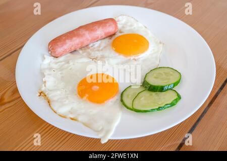 Œufs frits de deux œufs avec concombres et saucisses pour le petit déjeuner. Œufs frits, côté ensoleillé sur une assiette. Concept d'alimentation saine. Banque D'Images