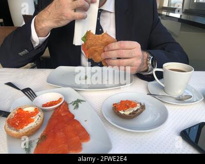 Homme dans un costume d'affaires, cravate et chemise blanche est de prendre le petit déjeuner, pause-café, une tasse de café, croissant avec saumon et salade verte, sandwichs avec Banque D'Images