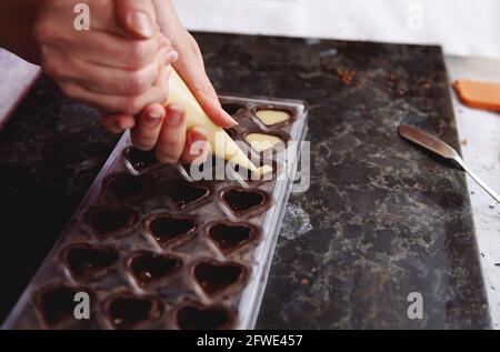 Gros plan sur le remplissage de la crème au caramel salé de confiserie mettre dans des moules de bonbons pour préparer des pralines au chocolat faites à la main Banque D'Images