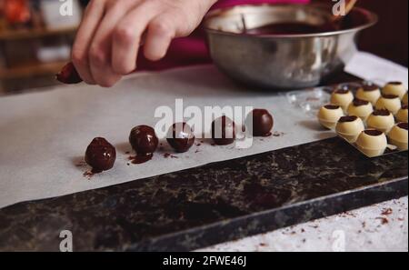 La dernière étape dans la préparation des truffes au chocolat belge dans la cuisine. Bonbons et ébauches prêts à l'emploi avec garnitures sur une table en marbre Banque D'Images