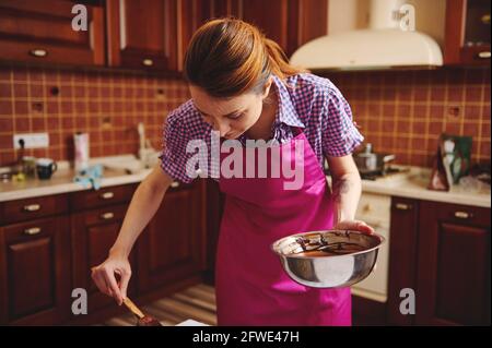 Jeune chef pâtissier travaillant à la préparation de chocolats faits à la main avec une masse de chocolat fondu dans sa cuisine. Fabrication de bonbons faits maison pour célébrer Banque D'Images