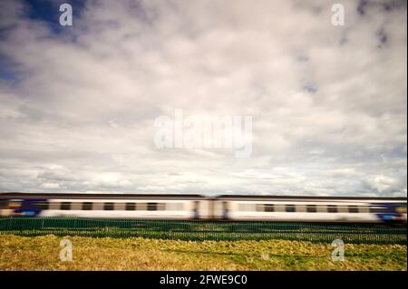 Train de voyageurs traversant les champs en milieu rural Banque D'Images