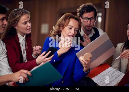 groupe d'employés de caucasiens essayant de présenter leur travail à leur patron qui utilise un rouge à lèvres dans un couloir Banque D'Images