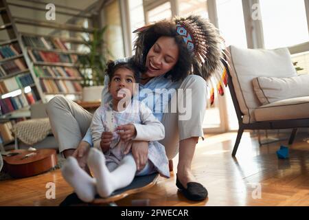 Une jeune maman avec une adresse indienne se déplace sur le skateboard avec sa petite fille dans une atmosphère joyeuse à la maison. Famille, ensemble, amour, jeu Banque D'Images