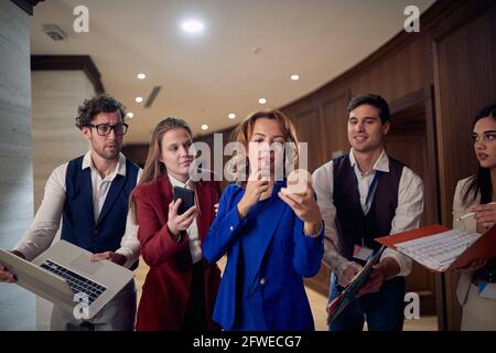 groupe d'employés de caucasiens essayant de présenter leur travail à leur patron qui met le rouge à lèvres dans un couloir Banque D'Images