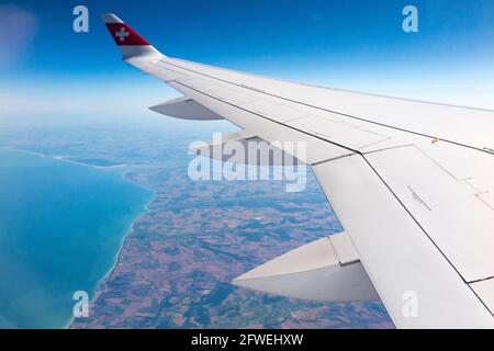 Ailes d'avion affichant le logo suisse drapeau / aile d'avion d'un Bombardier série C et la vue de la mer et de la côte depuis son altitude de croisière sur la côte de France par temps clair avec le ciel bleu. (100) Banque D'Images