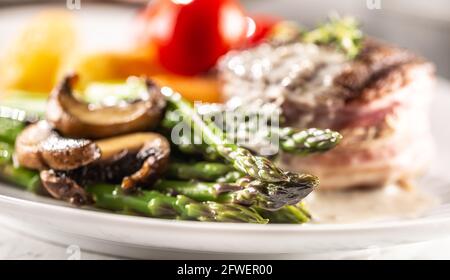 Steak grillé servi sur une assiette avec asperges, champignons et sauce. Banque D'Images