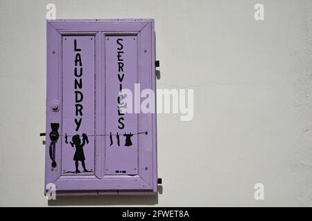 Service de blanchisserie panneau peint à la main sur un volet de fenêtre en bois lilas à Katapola, île d'Amorgos Cyclades, Grèce. Banque D'Images