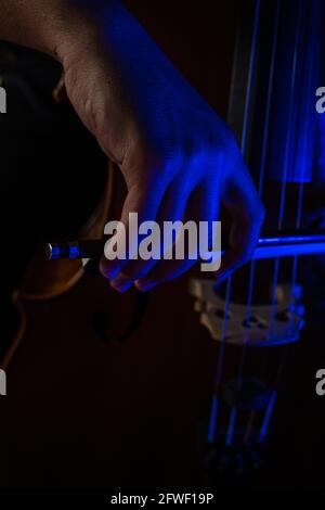 Photo artistique d'un jeune homme jouant le violoncelle où vous pouvez voir le détail de la main avec l'arc frottant les cordes avec la lumière bleue. Banque D'Images