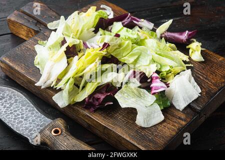 Mélanger les feuilles de salade, sur une planche à découper en bois, sur une ancienne table en bois sombre Banque D'Images