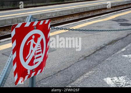 Un panneau métallique rouge placé au bord des voies ferrées d'une gare avertit les gens de rester à l'écart de la voie en raison du danger. Banque D'Images