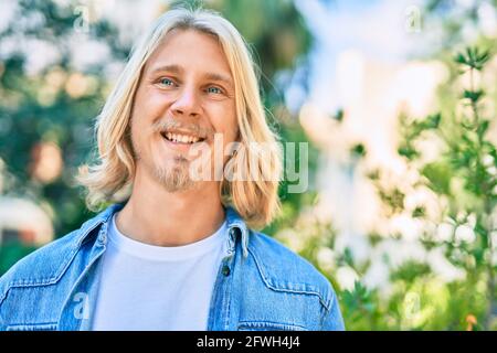 Jeune homme scandinave blond souriant heureux debout dans le parc. Banque D'Images