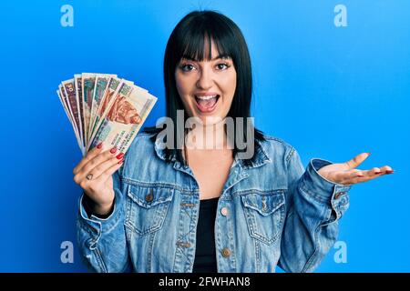 Une jeune femme hispanique détient des billets en livres égyptiennes célébrant sa réussite sourire heureux et expression du gagnant avec la main levée Banque D'Images