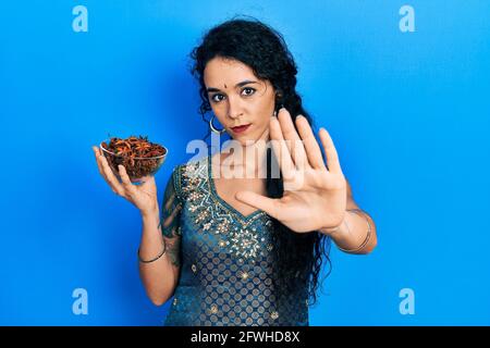 Jeune femme portant une robe bindi et kurta traditionnelle tenant un bol d'anis étoilé à main ouverte faisant signe d'arrêt avec une expression sérieuse et confiante, Banque D'Images