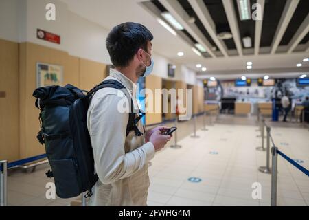 L'homme masqué utilise le téléphone et garde la distance dans la zone d'enregistrement pour les vols à l'aéroport de Chypre, dans la ville de Paphos, lors de l'enregistrement. Voyage en avion pendant le Covid Banque D'Images