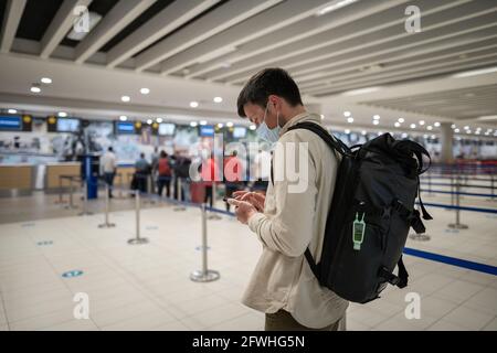 L'homme masqué utilise le téléphone et garde la distance dans la zone d'enregistrement pour les vols à l'aéroport de Chypre, dans la ville de Paphos, lors de l'enregistrement. Voyage en avion pendant le Covid Banque D'Images