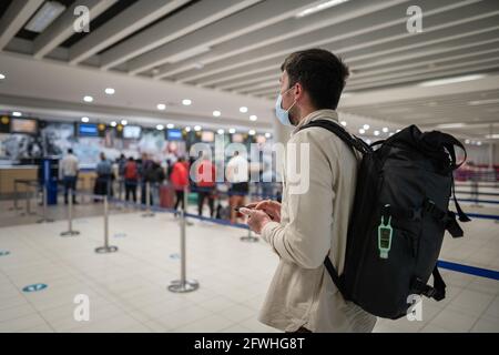 L'homme masqué utilise le téléphone et garde la distance dans la zone d'enregistrement pour les vols à l'aéroport de Chypre, dans la ville de Paphos, lors de l'enregistrement. Voyage en avion pendant le Covid Banque D'Images