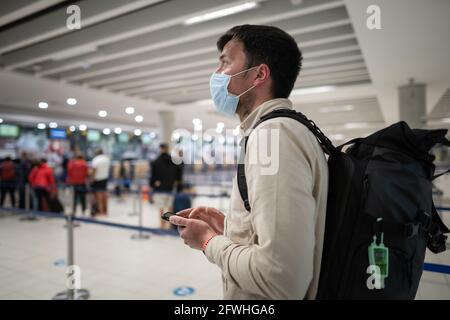 L'homme masqué utilise le téléphone et garde la distance dans la zone d'enregistrement pour les vols à l'aéroport de Chypre, dans la ville de Paphos, lors de l'enregistrement. Voyage en avion pendant le Covid Banque D'Images