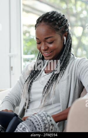 Jeune femme joyeuse avec des baids coiffure jeu de coiffure sur tablette ordinateur ou regarder un spectacle divertissant Banque D'Images