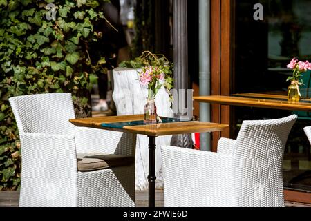 terrasse de café extérieure avec tables en bois et vase en verre et une fleur et chaises en osier devant le restaurant éclairé par soleil d'été avec siège vide Banque D'Images