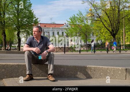 Un homme de race blanche adulte dans un T-shirt gris est assis et repose sur le trottoir Banque D'Images