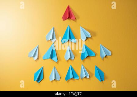 Avion de papier bleu origami suivant le rhe rouge sur fond jaune. Concept de leadership, de travail d'équipe et d'artisanat Banque D'Images